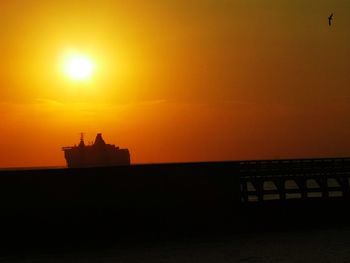 Silhouette built structure by sea against sky during sunset