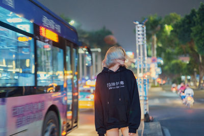 Young woman shaking head while standing on sidewalk in city at night