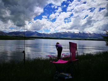 Rear view of man sitting by lake against sky