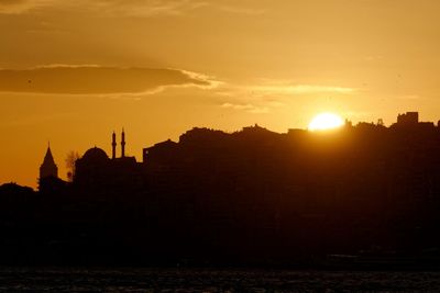 Scenic view of sea by silhouette buildings against sky during sunset