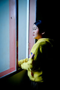 Side view of woman looking away while standing against window