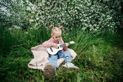 Little girl playing the ukulele in a blooming apple orchard in nature