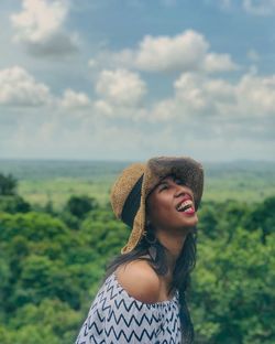 Young woman wearing hat laughing against landscape