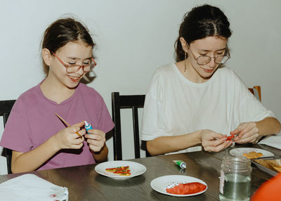 Two girl is coloring cookies while sitting at the table.