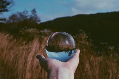 Cropped hand holding crystal ball against mountain with reflection