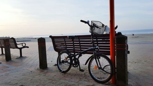 Bicycle on beach against sky during sunset