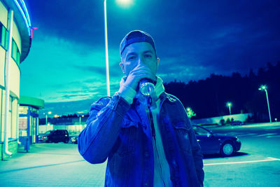Man standing at illuminated street against blue sky