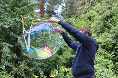 Man making bubbles with stick while standing against trees