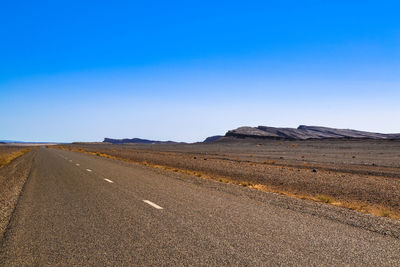 Road amidst desert against clear blue sky