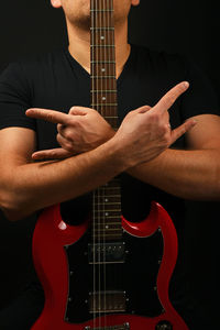 Midsection of man gesturing horn sign with guitar against black background