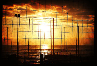 Reflection of sun on silhouette water against sky during sunset