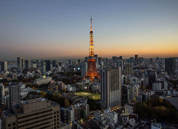 Illuminated tokyo tower in city against clear sky during sunset