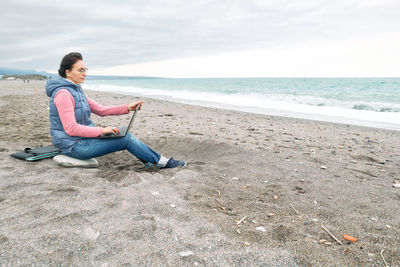 Beautiful sporty woman with laptop computer working outdoors while sitting on winter beach. 