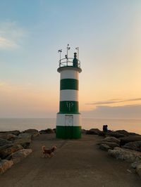 Lighthouse by sea against sky during sunset