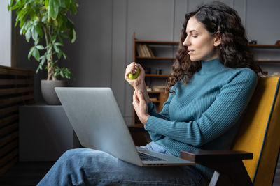 Female employee exercising with stress relieving silicone grip ring, relaxing from computer work