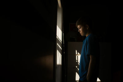 Young teen boy looking out the window during isolation