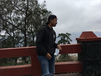 Side view of young man looking away against sky