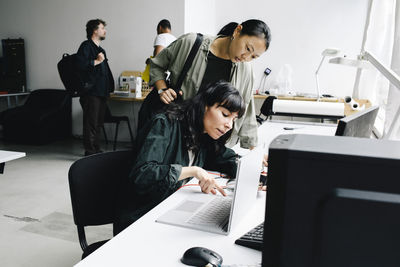 Female technician repairing laptop while sitting near customer at store