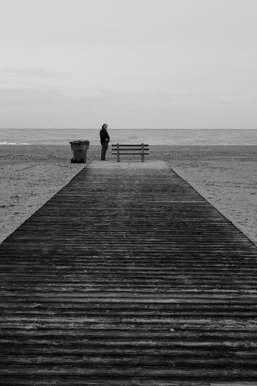 REAR VIEW OF MAN ON PIER OVER SEA