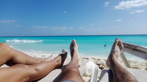 Low section of man and woman relaxing on beach against sky