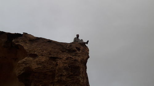 Low angle view of man standing on rock against sky