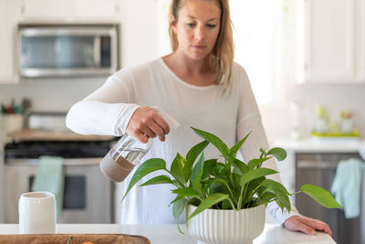 Woman spraying water on plants at home