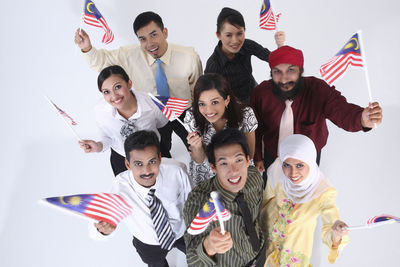 High angle portrait of smiling business people holding malaysian flag while standing over white background
