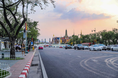 Cars on city street against sky during sunset