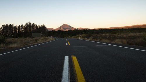 Road leading towards mountain against clear sky