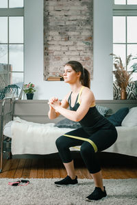 A strong and beautiful sports fitness girl in sportswear doing squats with sports fitness bands 