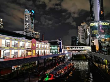 Illuminated buildings by river against sky in city at night