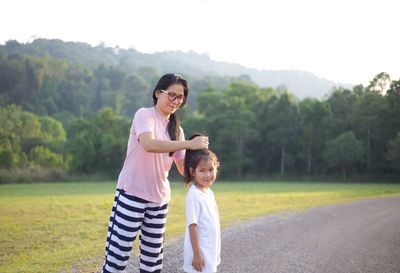 Mother tying hair of daughter while standing on road