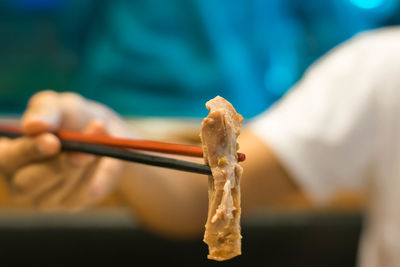 Midsection of person holding meat on chopsticks