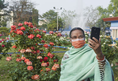 Face mask wearing  bengali woman taking selfie during her visit at rabindra sarobar flower show.