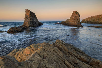 Scenic view of rocks on beach against sky during sunset