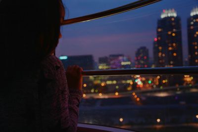 Side view of girl looking through window in city at night