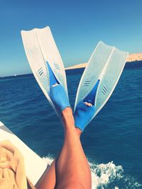 Low section of woman wearing diving flippers in boat on sea against blue sky