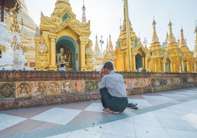 Rear view of man sitting outside temple against building