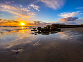 Reflecting sunset off sand and rocks with clouds at swamis beach in encinitas, san diego, california