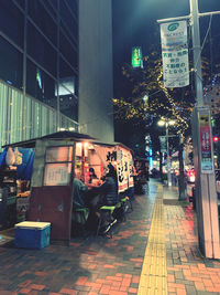 People on illuminated street amidst buildings in city at night