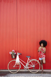 Young woman standing by bicycle in front of red wall