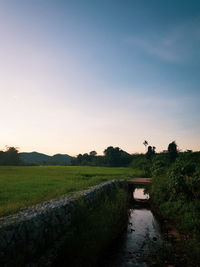 Canal amidst field against sky during sunset