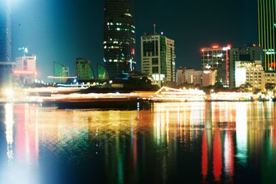 Illuminated city by river against clear sky at night