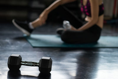 Close-up of dumbbell with woman sitting on floor at gym