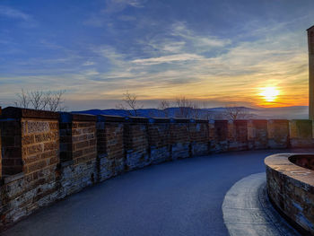 Footpath by wall against sky during sunset