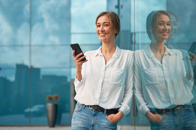 Smiling young woman using smart phone while standing on laptop