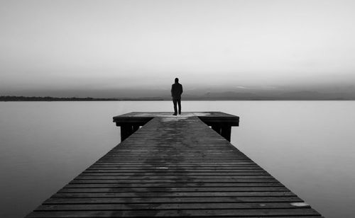 Rear view of man standing on pier at sea against clear sky