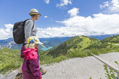 Side view of mother and daughter walking on mountain against cloudy sky