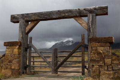 Wooden chained ranch gate and stone pillars against background of mountains in dark cloudy weather
