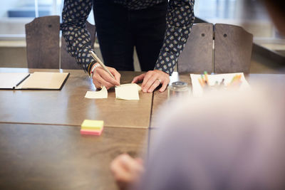 Midsection of businessman writing on adhesive note at conference table in office